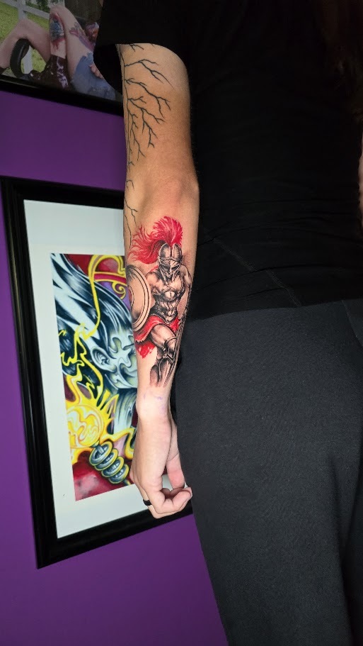 Black and grey Spartan forearm tattoo with red accents by Billy Smith