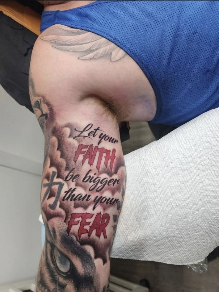 Black and grey faith over fear upper arm tattoo with red lettering by Miguel Ramos