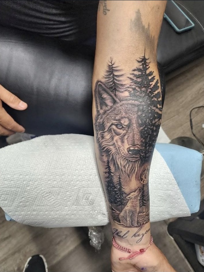 Black and grey wolf and pine forest forearm tattoo by Miguel Ramos